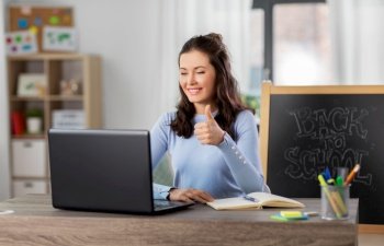 distant education, school and people concept - happy smiling female teacher with laptop computer having online class at home showing thumbs up. teacher with laptop having online class at home