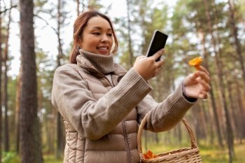 technology, leisure and people concept - young asian woman with smartphone using app to identify mushroom in autumn forest. asian woman using smartphone to identify mushroom