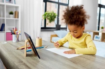 childhood, creativity and art concept - little african american girl with coloring pencils drawing picture on paper at home. little girl drawing with coloring pencils at home