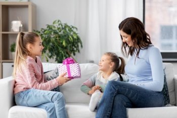 people, family and holidays concept - happy girl giving birthday present to younger sister at home. girl giving present to younger sister at home
