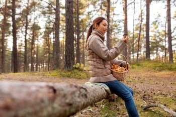picking season, leisure and people concept - young asian woman with mushrooms in basket in autumn forest. woman with mushrooms in basket in autumn forest