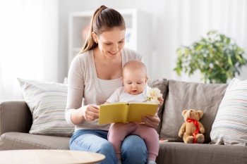 family, motherhood and people concept - happy smiling mother reading book to little baby daughter at home. happy mother reading book to little baby at home