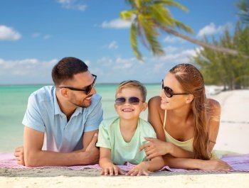 family, travel and tourism concept - happy mother, father and little son in sunglasses lying on blanket over tropical beach background in french polynesia. happy family lying over tropical beach background