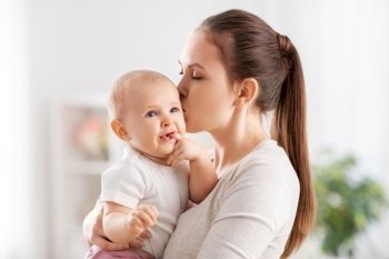 family, motherhood and people concept - happy mother kissing her little baby daughter at home. happy mother kissing little baby daughter at home