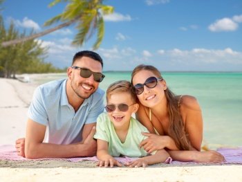 family, travel and tourism concept - happy mother, father and little son in sunglasses lying on blanket over tropical beach background in french polynesia. happy family lying over tropical beach background