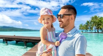 family, fatherhood and travel concept - happy smiling father with little daughter on wooden bridge over tropical beach background in french polynesia. happy father with little daughter on beach