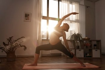 sport, fitness and people concept - happy pregnant woman doing yoga reverse warrior pose at home over sunshine. pregnant woman doing yoga at home over sunshine