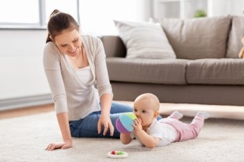 family, motherhood and people concept - happy smiling mother and little baby daughter playing with soft ball toy on floor at home. happy smiling mother with little baby at home
