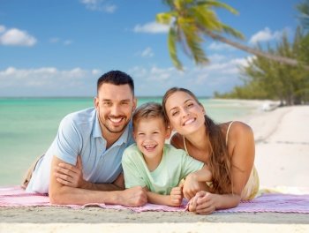 family, travel and tourism concept - happy mother, father and little son lying on blanket over tropical beach background in french polynesia. happy family lying over tropical beach background