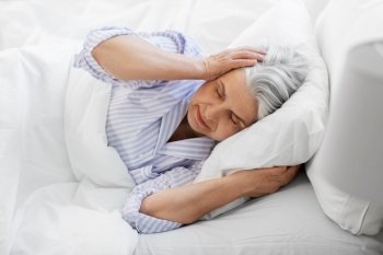 bedtime, rest and old people concept - annoyed senior woman in pajamas suffering from headache lying in bed at home bedroom. annoyed senior woman with headache in bed at home