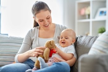 family, motherhood and people concept - happy smiling mother and little baby playing with teddy bear toy at home. mother with baby playing with teddy bear at home