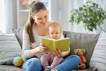 family, motherhood and people concept - happy smiling mother reading book to little baby daughter at home. happy mother reading book to little baby at home