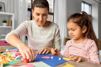 family, art and craft concept - mother spending time with her little daughter making applique of color paper at home. daughter with mother making applique at home