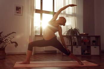 sport, fitness and people concept - happy pregnant woman doing yoga reverse warrior pose at home over sunshine. pregnant woman doing yoga at home over sunshine
