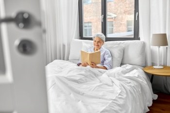 old age, leisure and people concept - senior woman reading book in bed at home bedroom. senior woman reading book in bed at home bedroom
