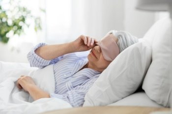 old age and people concept - senior woman with eye sleeping mask in bed at home bedroom. senior woman with eye sleeping mask in bed at home