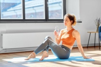 fitness, people and healthy lifestyle concept - woman with bottle of water resting on yoga mat at home or studio. woman with water resting on yoga mat at home