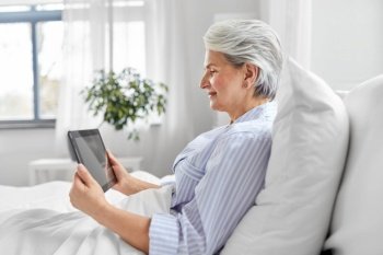 technology, old age and people concept - senior woman with tablet pc computer in bed at home bedroom. senior woman with tablet pc in bed at home bedroom