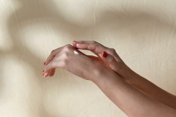 beauty product, cosmetics and people concept - female hands applying moisturizer to skin on beige background. female hands applying moisturizer to skin