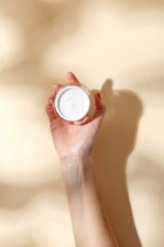beauty product, cosmetics and people concept - female hand holding jar of moisturizer on beige background. female hand holding jar of moisturizer
