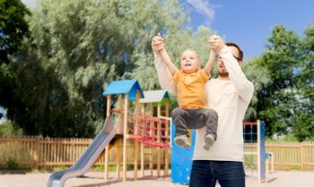 family, childhood, fatherhood, leisure and people concept - happy father and little son playing and having fun over children’s playground background. father with son playing and having fun