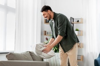 household, home improvement and cleaning concept - happy smiling man arranging cushions on sofa. happy smiling man arranging sofa cushions at home