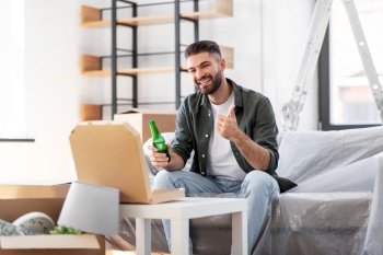 moving, people and real estate concept - happy smiling man with box of pizza and beer bottle at new home showing thumbs up. man with box of pizza and beer bottle at new home
