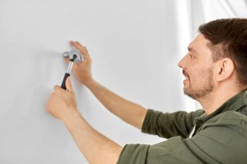 home improvement, repair and people concept - happy smiling man hammering nail to wall. smiling man hammering nail to wall at home