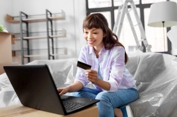 moving, people and real estate concept - happy smiling asian woman with laptop computer and credit card at new home. woman with laptop and credit card at new home