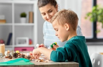 family, creativity and craft concept - mother and little son with glue sticks and paper making pictures of dry autumn leaves, pine cones and chestnuts at home. mother and son making pictures of autumn leaves