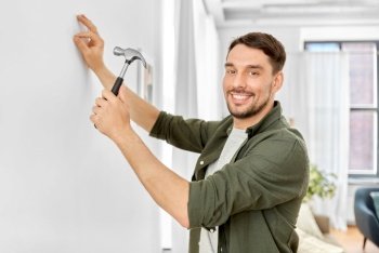 home improvement, repair and people concept - happy smiling man hammering nail to wall. smiling man hammering nail to wall at home