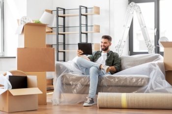 moving, people and real estate concept - happy smiling man with tablet pc computer and boxes at new home. man with tablet pc and boxes moving into new home