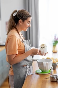 culinary, baking and people concept - happy smiling young woman cooking food on kitchen at home with cupcakes making topping of whipped cream or mascarpone cheese. woman cooking food and baking on kitchen at home