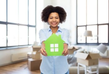 moving, real estate and people concept - happy smiling african american young woman with green house icon over new home background. african woman with green house icon at new home