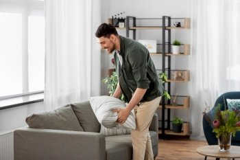 household, home improvement and cleaning concept - happy smiling man arranging cushions on sofa. happy smiling man arranging sofa cushions at home