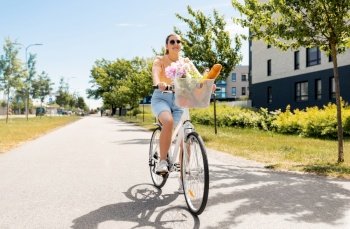 people, leisure and lifestyle - happy young woman with food and flowers in basket of bicycle on city street. woman with food and flowers in bicycle basket
