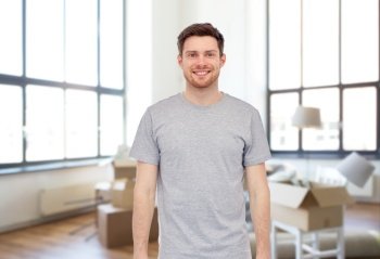 moving, real estate and people concept - happy smiling young man in gray t-shirt and jeans over new home background. smiling young man in gray t-shirt at new home