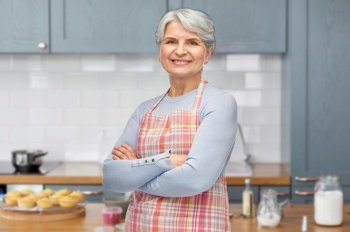 cooking, culinary and old people concept - portrait of smiling senior woman in apron over home kitchen background. portrait of smiling senior woman at kitchen