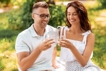 leisure and people concept - happy couple with drinks having picnic at summer park. happy couple toasting drinks at summer park