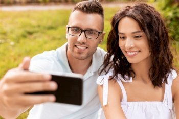 leisure and people concept - happy couple having picnic and taking selfie with smartphone at summer park. happy couple taking selfie at summer park
