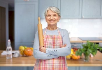 cooking, culinary and old people concept - smiling senior woman in apron with rolling pin over home kitchen background. smiling senior woman in apron with rolling pin