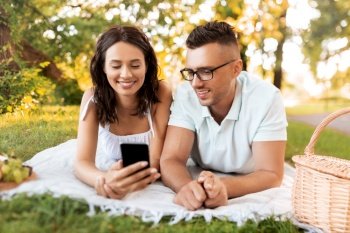 leisure and people concept - happy couple with smartphone having picnic at summer park. happy couple with smartphone at picnic in park