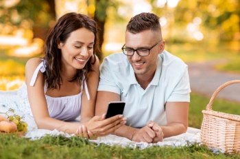 leisure and people concept - happy couple with smartphone having picnic at summer park. happy couple with smartphone at picnic in park