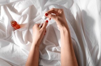 beauty product, cosmetics and people concept - female hands with dropper applying serum to skin over white sheet with folds. female hands with dropper applying serum to skin