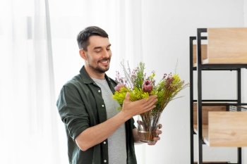 home improvement, decoration and people concept - happy smiling man placing flower in vase or houseplant to shelf. man decorating home with flower or houseplant
