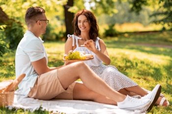 leisure and people concept - happy couple with food having picnic at summer park. happy couple having picnic at summer park