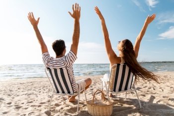 leisure, relationships and people concept - happy couple with picnic basket sitting in folding chairs on summer beach. happy couple sitting in folding chairs on beach