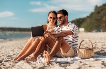 leisure and people concept - happy couple with tablet pc computer and picnic basket on summer beach. happy couple with tablet pc at picnic on beach