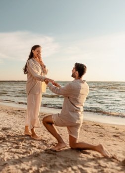 love and people concept - smiling young man with engagement ring making proposal to happy woman on beach. man with ring making proposal to woman on beach