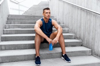 fitness, sport and people concept - tired young man with bottle of isotonic energy drink sitting on stairs. tired sportsman with bottle sitting on stairs